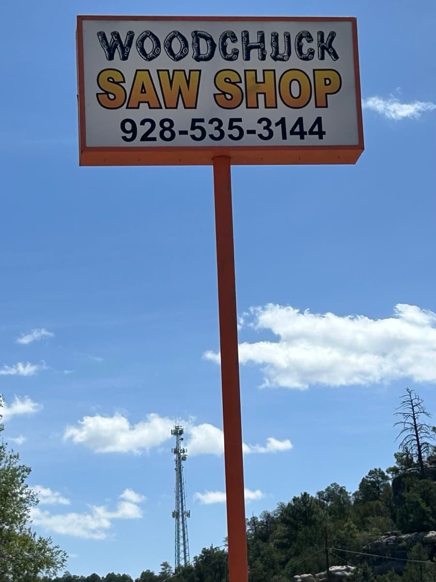 Tall orange pole sign reading WOODCHUCK SAW SHOP 928-535-3144 against an Arizona blue sky